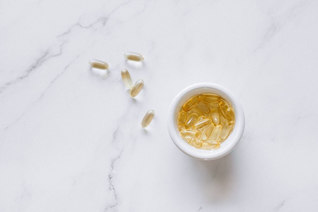 Golden softgel supplement capsules in a small white bowl on a marble surface, with a few capsules scattered alongside