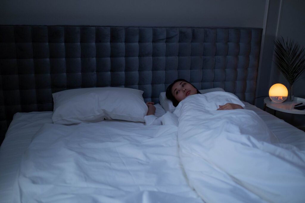 Woman lying awake in a dimly lit bedroom in the middle of the night, a glowing bedside clock on the nightstand beside her