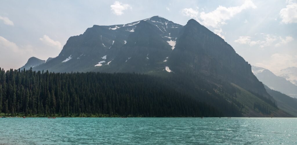 Hazy, smoke-filled mountain valley with a turquoise lake below, the sky and peaks dimmed by distant wildfire haze.