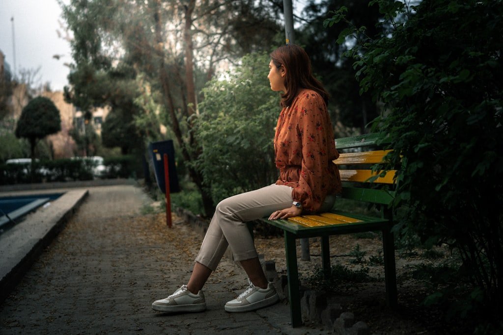 A woman sits alone on a park bench in quiet reflection, representing the private emotional processing many parents experience during the back-to-school transition.