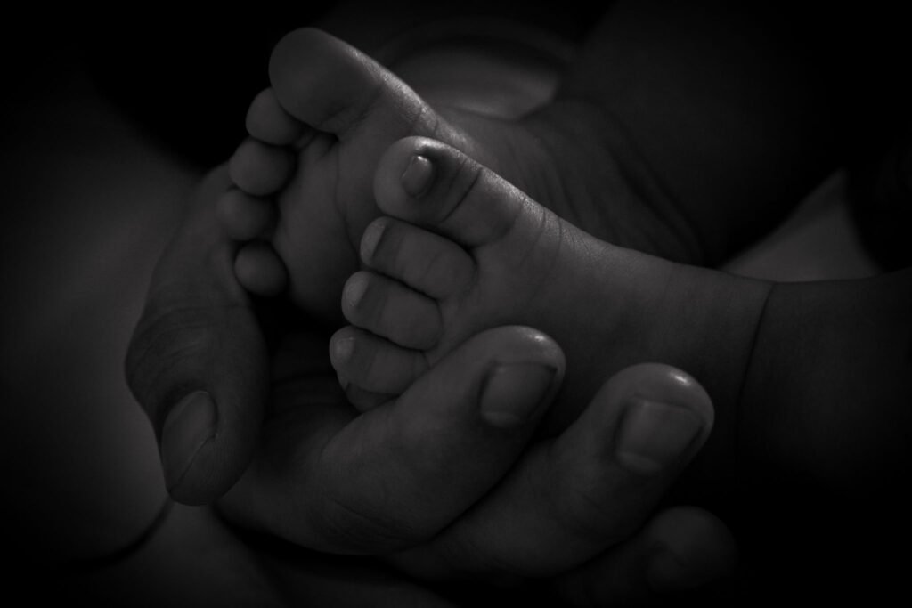Close-up black and white photo of a mother tenderly cradling her newborn baby's bare foot in her hands
